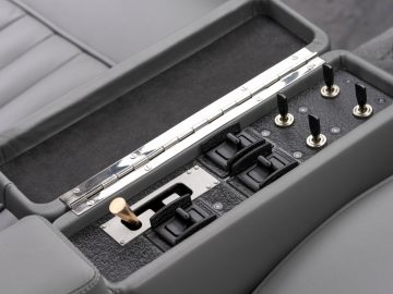 Een zilveren fluit opgeborgen in een open, gevoerde koffer tussen twee grijze Aston Martin DB5 Goldfinger Continuation-autostoelen.