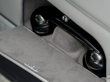 Close-up van het interieur van een Aston Martin DB5 Goldfinger Continuation-autodeur met een luidspreker en bedieningsknoppen, met de nadruk op het paneel met structuurstof.