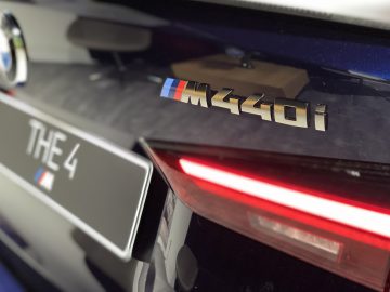 Close-up van de achterkant van een auto met een BMW 4 Serie Coupé-logo, een aangepast plaatje met het opschrift 'The 4' en een abstract designdetail op de kofferbak.