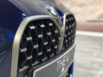 Close-up van een blauwe BMW 4 Serie Coupé-voorgrille en badge, met een focus op de textuur en details van de grille.
