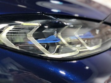 Close-up van de led-koplamp van een moderne BMW 4 Serie Coupé op een blauw voertuig, met de nadruk op het ingewikkelde ontwerp en de helderheid van de koplampcomponenten.