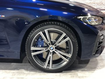 Close-up van het stuur en het linker voorspatbord van een BMW 4 Serie Coupé, met een meerspaaks lichtmetalen velg en het m-logo.