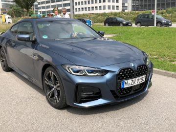 Een blauwe BMW 4 Serie Coupé geparkeerd in een stadsstraat met lopende mensen op de achtergrond.