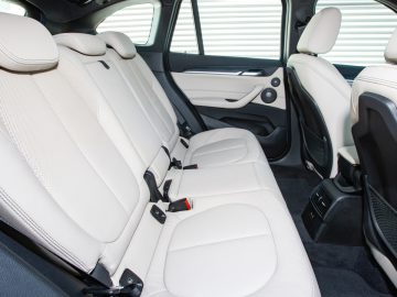 Interieur van een BMW X1 met witleren achterbank, een middenarmsteun achterin en zwart-witte deurpanelen.