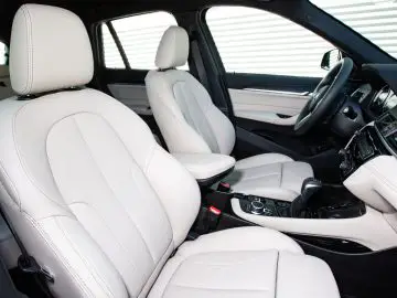 Interieur van een moderne BMW X1 met witte lederen stoelen, een dashboard en een middenconsole met automatische transmissie.