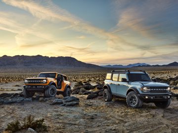 Twee moderne Ford Broncos geparkeerd op een rotsachtig woestijnlandschap bij zonsondergang.