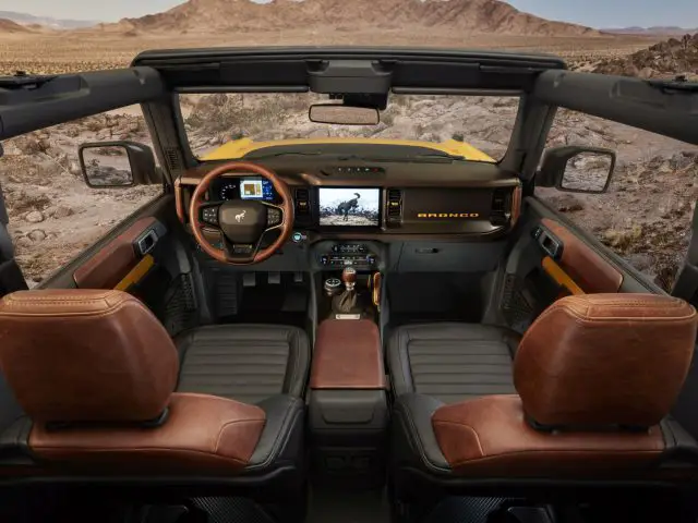 Binnenaanzicht van een Ford Bronco, met het dashboard, het stuur en de lederen stoelen, met een woestijnlandschap zichtbaar door de voorruit.