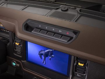 Een weergave van het dashboard van een Ford Bronco met een digitaal display met een 3D-model van een dinosaurus, ventilatieopeningen en bedieningsknoppen.
