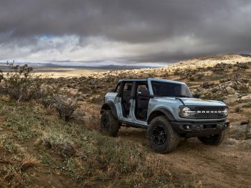 Een Ford Bronco geparkeerd op een rotsachtig pad met een stormachtige lucht erboven en een uitgestrekt woestijnlandschap op de achtergrond.