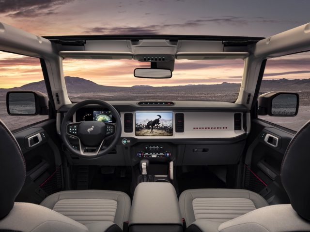 Binnenaanzicht van een Ford Bronco, met een modern dashboard en stuur, met een woestijnlandschap zichtbaar door de voorruit.