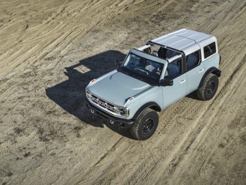 Luchtfoto van een witte Ford Bronco geparkeerd op zanderig terrein, met zijn robuuste ontwerp en open dak.
