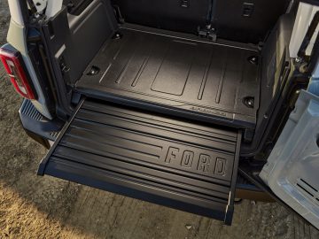 Achteraanzicht van een open bagageruimte in een Ford Bronco met een uitgeschoven metalen schuiflade, weergegeven op een vuil oppervlak.