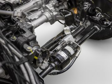 Close-up van het ophangingssysteem en de stuurcomponenten van een Ford Bronco, met gedetailleerde mechanische onderdelen op een grijze achtergrond.
