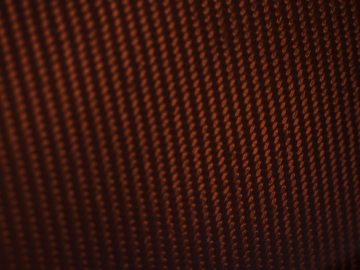 Close-up van een gestructureerd oppervlak met talloze kleine, verlichte oranje stippen op de Donkervoort D8 GTO-JD70 Bare Naked Carbon Edition, waardoor een abstract patroon ontstaat.
