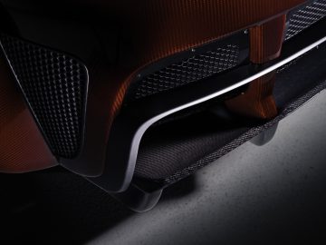 Close-up van de achterkant van een Donkervoort D8 GTO-JD70 Bare Naked Carbon Edition met een gedetailleerd beeld van de koolstofvezeltextuur en het uitlaatsysteem.