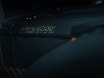 Close-up van het dashboard van een Donkervoort D8 GTO-JD70 Bare Naked Carbon Edition met embleem verlicht bij weinig licht.