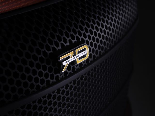 Close-up van een '710 pk'-badge op een Donkervoort D8 GTO-JD70 Bare Naked Carbon Edition-autogrille met een gaaspatroon.