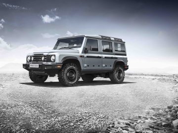 Een INEOS Grenadier geparkeerd op een grindoppervlak met wolken op de achtergrond.