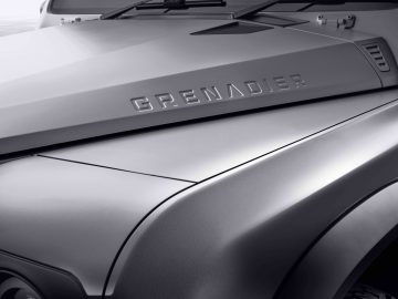 Close-up van de motorkap van een voertuig met de naam "INEOS Grenadier" erop gedrukt.
