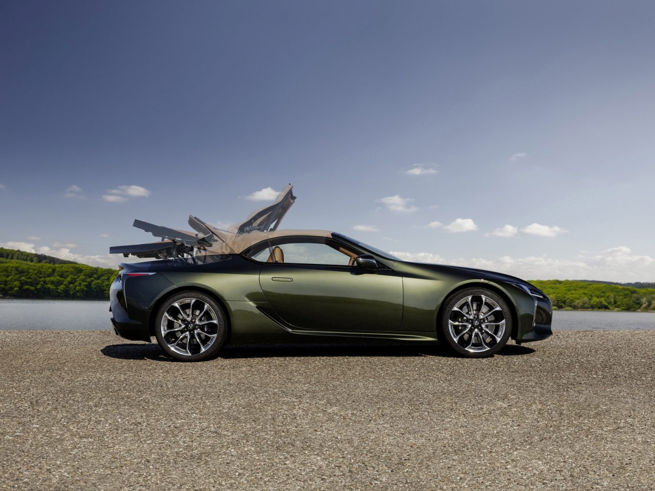 Een groene Lexus LC Convertible met de deuren naar boven open, geparkeerd aan de oever van een meer onder een helderblauwe lucht.