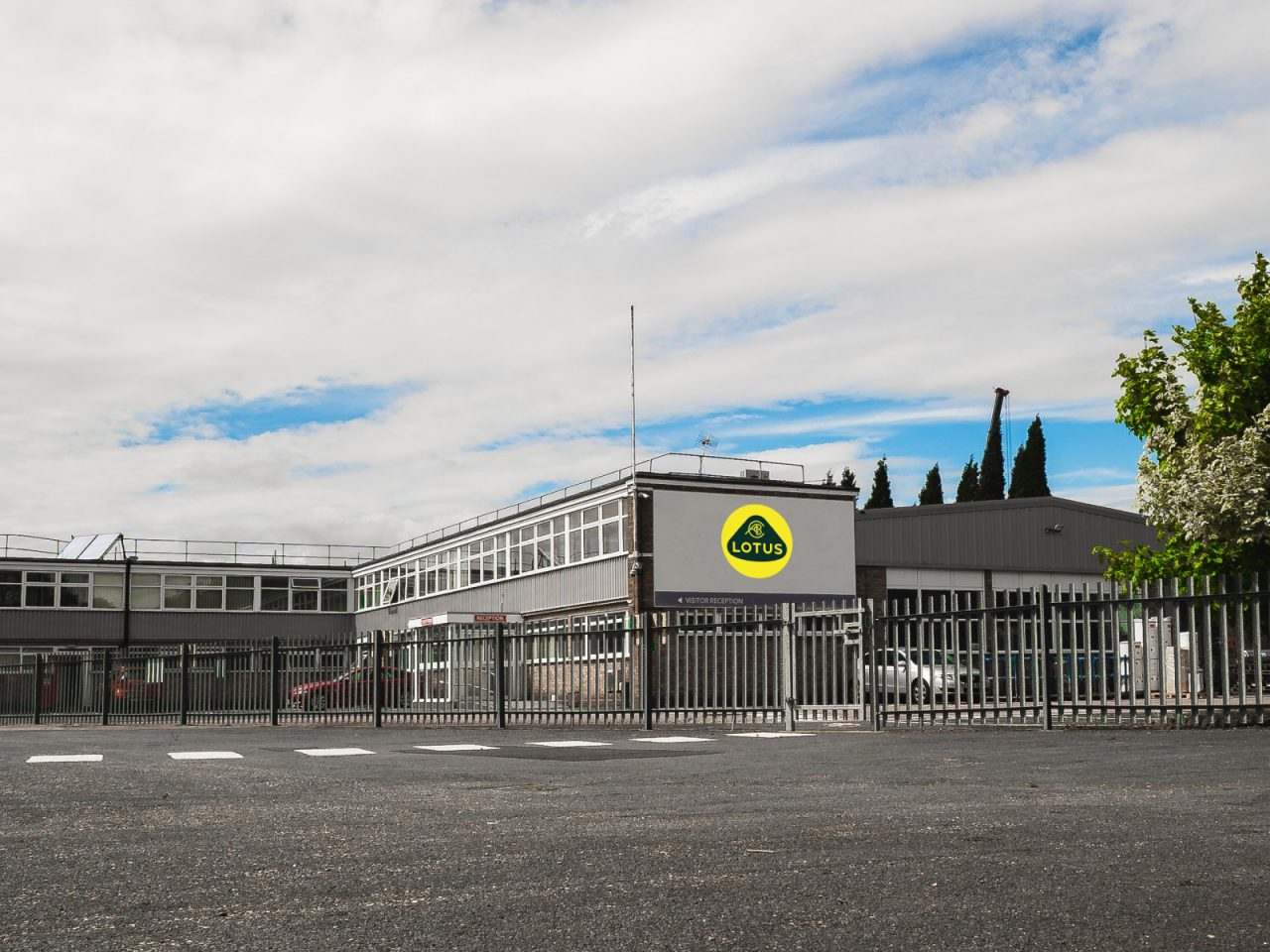 Buitenaanzicht van de Lotus-faciliteit met bedrijfslogo weergegeven, beveiligd door een metalen hek onder een bewolkte hemel.