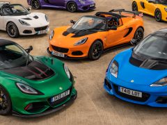 Een verzameling van vijf kleurrijke Lotus-sportwagens geparkeerd op beton, met verschillende modellen in wit, oranje, groen, blauw en geel.