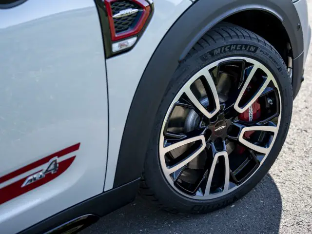 Close-up van het achterwiel van een MINI John Cooper Works Countryman met rode remklauwen en Michelin-banden, met een gedetailleerd lichtmetalen velgontwerp.