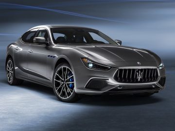 Een slanke grijze Maserati Ghibli Hybrid sedan geparkeerd in een studioomgeving, met zijn opvallende grille en blauwe remklauwen.