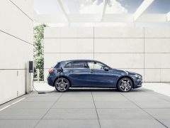 Een blauwe elektrische auto van Mercedes-Benz A-Klasse laadt op bij een station op een moderne parkeerplaats met witte muren en groen aan de zijkant.