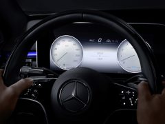 Handen van de bestuurder op het stuur van een Mercedes-Benz S-Klasse met zicht op de digitale snelheidsmeter en dashboardbediening 's nachts.