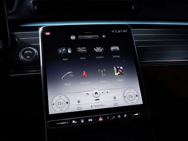 Binnenaanzicht van een Mercedes-Benz S-Klasse met een groot touchscreen-dashboard met verschillende pictogrammen voor navigatie, media en voertuiginstellingen.