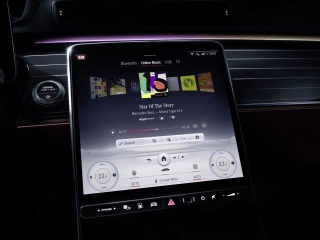 Binnenaanzicht van een Mercedes-Benz S-Klasse met een groot touchscreen dashboarddisplay met multimediabediening en temperatuurinstellingen die 's nachts verlicht zijn.