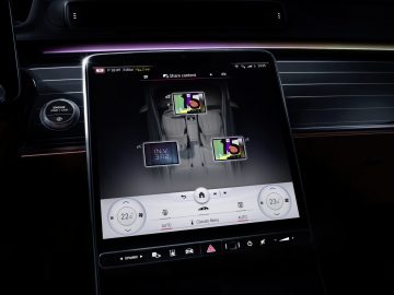 Binnenaanzicht van een Mercedes-Benz S-Klasse, gericht op de middenconsole met een touchscreen met multimediapictogrammen en sfeerverlichting.