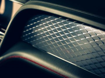 Close-up van het binnendeurpaneel van een Bentley Bentayga met een geometrisch patroon en contrasterende stiksels.