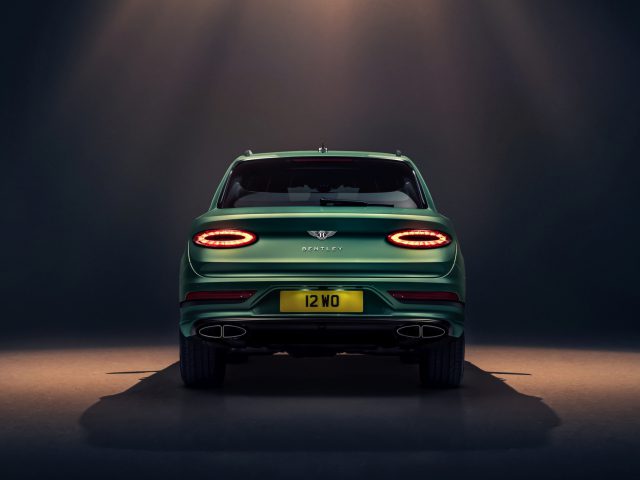 Achteraanzicht van een groene Bentley Bentayga met verlichte achterlichten tegen een donkere achtergrond met bovenverlichting.