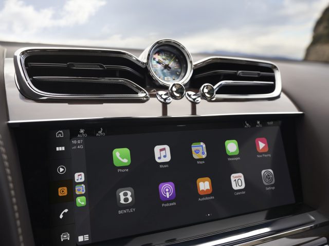 Luxe Bentley Bentayga-interieur met infotainment-aanraakscherm met smartphone-integratie-apps en een elegante analoge klok erboven.