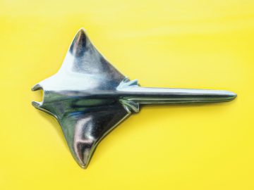 Een glanzend metallic Opel Manta-vormig object op een felgele achtergrond.