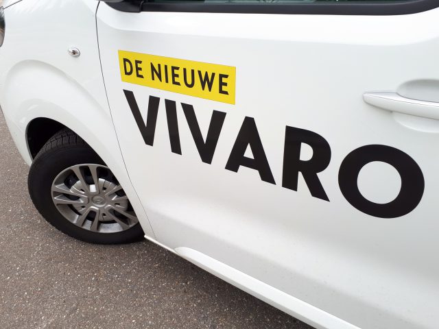 Zijaanzicht van een witte Opel Vivaro-bestelwagen met de tekst "de nieuwe vivaro" in het zwart op de deur gedrukt.