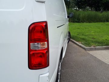 Witte Opel Vivaro-bestelwagen geparkeerd langs de weg, met een close-up van de achterlichten en een gedeeltelijk zicht op de zijspiegel.