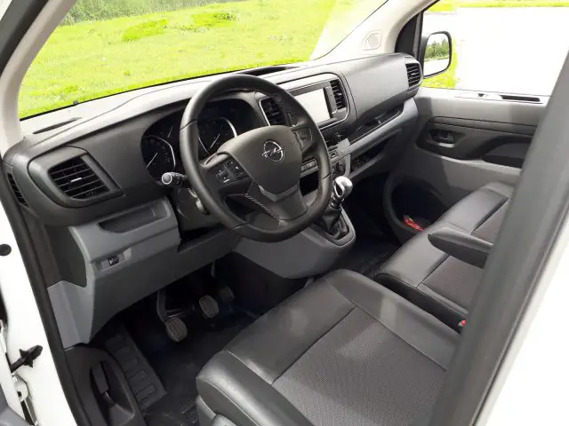 Binnenaanzicht van een Opel Vivaro met de bestuurdersstoel, het stuur met logo, het dashboard en de geopende voordeur.