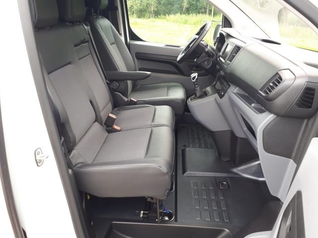 Interieur van een Opel Vivaro met bestuurdersstoel, passagiersstoel, stuur, dashboard en open deur.