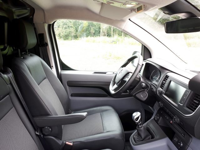 Binnenaanzicht van een Opel Vivaro met de bestuurdersstoel, het stuur, het dashboard en een handgeschakelde versnellingsbak.