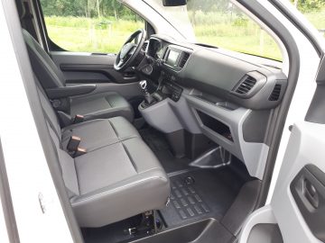 Binnenaanzicht van een Opel Vivaro met de bestuurderszijde met een open deur, met het stuur, het dashboard en de stoelen.
