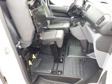 Interieur van een Opel Vivaro met aangepaste zitplaatsen in een bestelwagen met adaptieve uitrusting voor toegankelijkheid, inclusief gespecialiseerde vloerrails en harnassen.