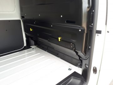 Lege laadruimte van een Opel Vivaro-bestelwagen met een open deur, met een schoon, overzichtelijk metalen interieur met gele handgrepen.