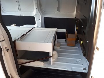 Achteraanzicht van een Opel Vivaro met een geopende deur met daarin een gedemonteerd bureau en een kleine kartonnen doos erin.