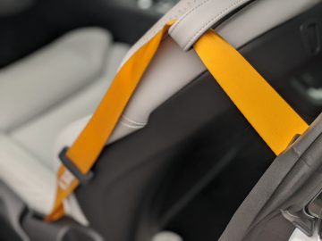 Gele veiligheidsgordel over een witte autostoel in het interieur van een Polestar 1-voertuig, gefocust op de gordel met een onscherpe achtergrond.