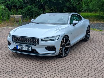 Een witte Polestar 1 luxecoupé geparkeerd op een bakstenen oppervlak, met een strak ontwerp en een moderne grille met het kenteken ‘orp 84k.