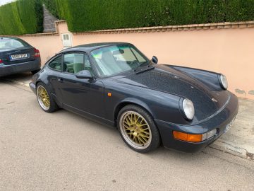 Een donkerblauwe Porsche 911 met gouden wielen, gemeld als 'auto gestolen', geparkeerd in een straat naast een trottoir.