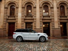 Witte Range Rover geparkeerd op een geplaveide straat voor een klassiek gebouw met boogramen en een rode deur.